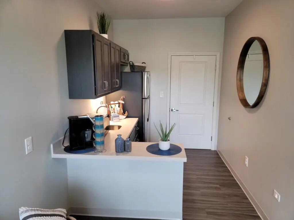 kitchenette with peninsula countertop, coffee machine, mugs, sink, cabinets, and fridge